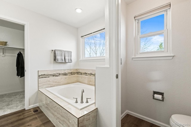 bathroom featuring a garden tub, wood finished floors, a walk in closet, and baseboards