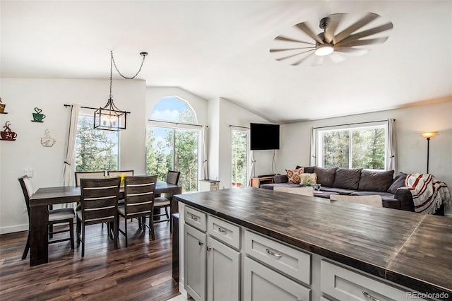 kitchen with pendant lighting, butcher block countertops, ceiling fan with notable chandelier, vaulted ceiling, and dark hardwood / wood-style flooring