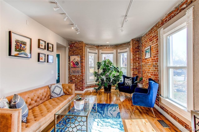 living room featuring visible vents, brick wall, track lighting, and hardwood / wood-style flooring