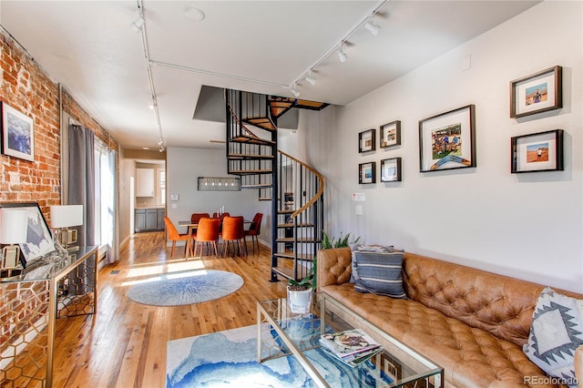 living room featuring stairway, rail lighting, brick wall, and wood finished floors