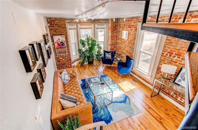 living area featuring hardwood / wood-style floors, visible vents, brick wall, and rail lighting