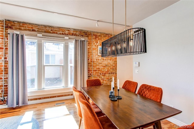 dining room with visible vents, track lighting, brick wall, baseboards, and wood finished floors