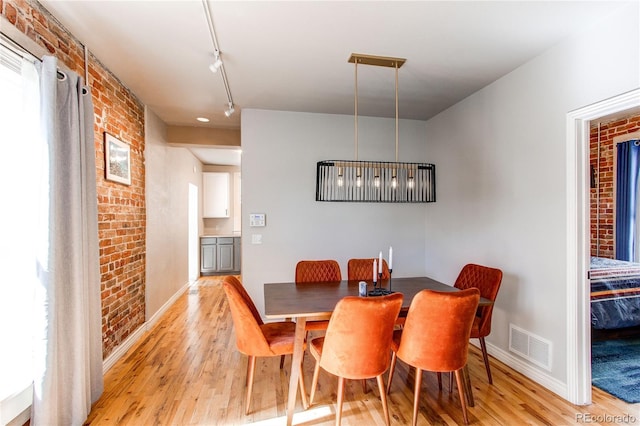 dining room featuring light wood-style flooring, visible vents, and brick wall