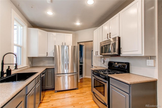 kitchen featuring light wood finished floors, gray cabinets, a sink, stainless steel appliances, and white cabinetry