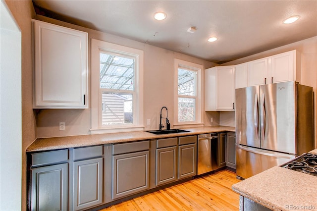 kitchen with light wood finished floors, light countertops, appliances with stainless steel finishes, white cabinets, and a sink