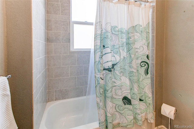 full bath with a textured wall and shower / tub combo with curtain