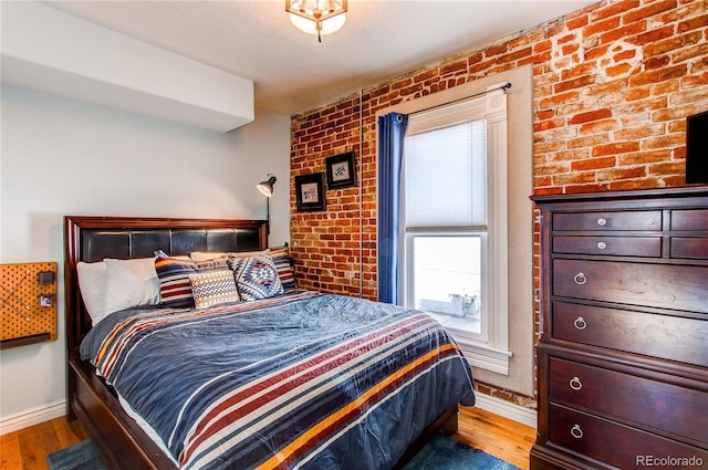 bedroom with baseboards, wood finished floors, and brick wall