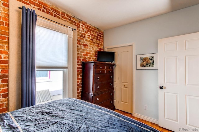 bedroom featuring wood finished floors, baseboards, and brick wall