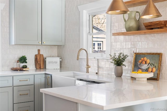 kitchen featuring open shelves, decorative backsplash, a sink, gray cabinets, and light stone counters