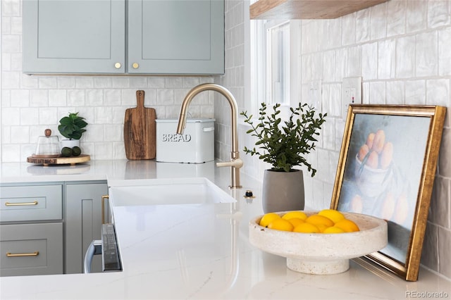kitchen view of gray cabinetry, backsplash, and light stone countertops