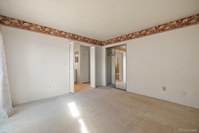 unfurnished bedroom with two closets, light colored carpet, and a textured ceiling