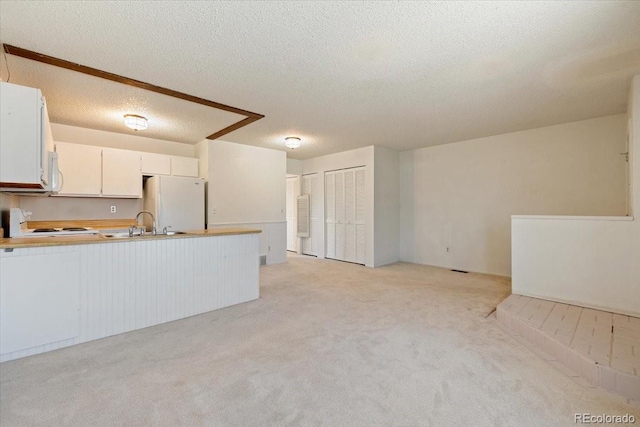 kitchen with sink, white cabinets, white appliances, light carpet, and a textured ceiling