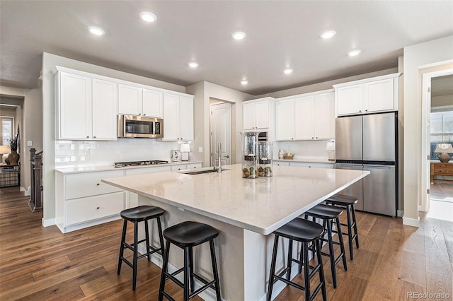 kitchen with a large island with sink, a kitchen bar, dark wood-type flooring, white cabinetry, and stainless steel appliances