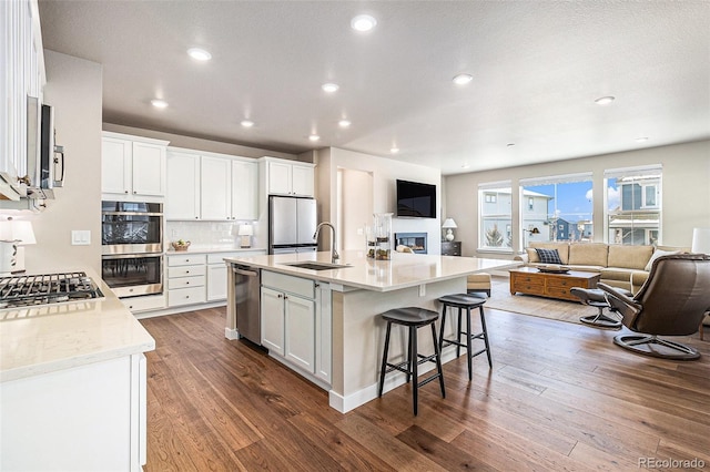 kitchen featuring a center island with sink, decorative backsplash, sink, stainless steel appliances, and white cabinets