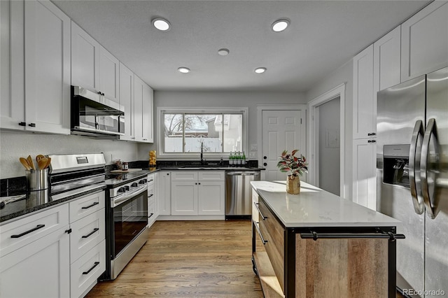 kitchen featuring stainless steel appliances, light hardwood / wood-style flooring, sink, dark stone counters, and white cabinets