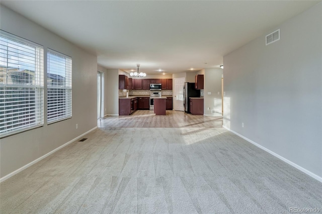 unfurnished living room featuring sink, light carpet, and an inviting chandelier