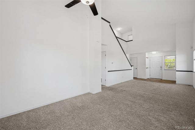 unfurnished living room with carpet floors, a ceiling fan, baseboards, and a high ceiling