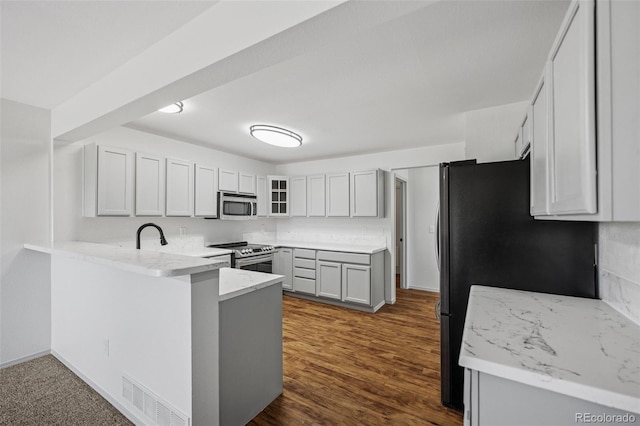 kitchen featuring stainless steel appliances, a peninsula, dark wood-style flooring, light stone counters, and glass insert cabinets
