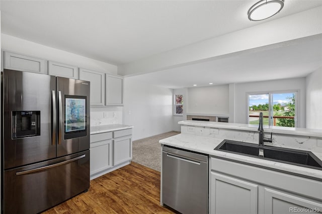 kitchen featuring stainless steel appliances, a sink, light stone countertops, and dark wood-type flooring