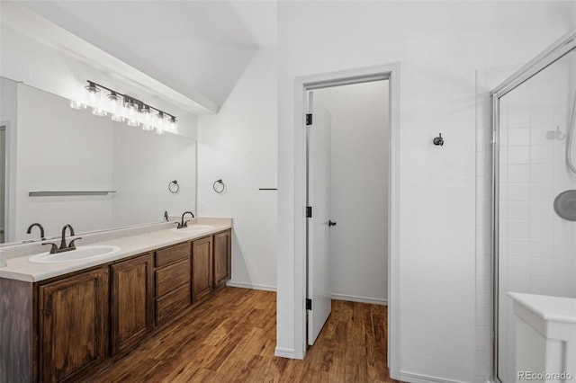 full bathroom with wood finished floors, double vanity, baseboards, and tiled shower