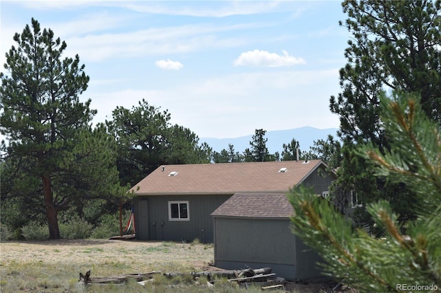 view of property exterior with a shingled roof and a mountain view