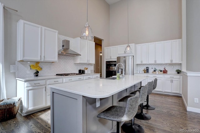 kitchen featuring a breakfast bar, appliances with stainless steel finishes, white cabinets, wall chimney range hood, and a towering ceiling