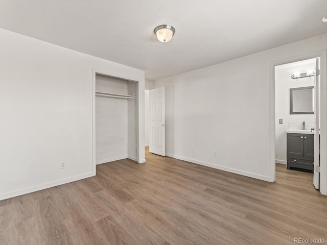 unfurnished bedroom featuring sink, connected bathroom, light wood-type flooring, and a closet