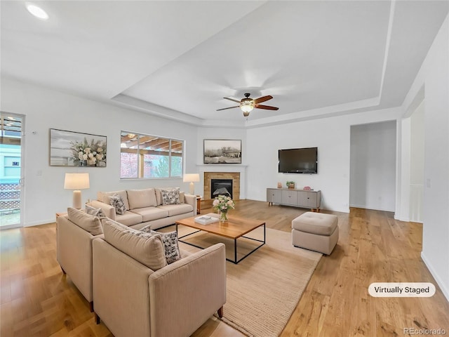 living room featuring ceiling fan, light hardwood / wood-style floors, and a raised ceiling