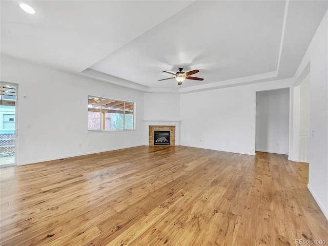 unfurnished living room featuring light hardwood / wood-style floors, ceiling fan, a raised ceiling, and a tiled fireplace