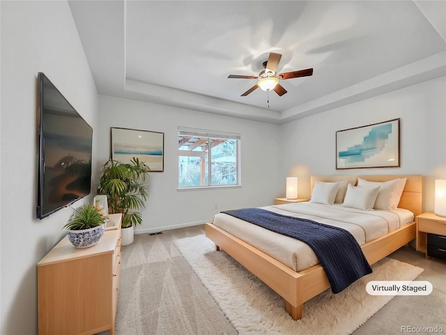 carpeted bedroom featuring ceiling fan and a tray ceiling