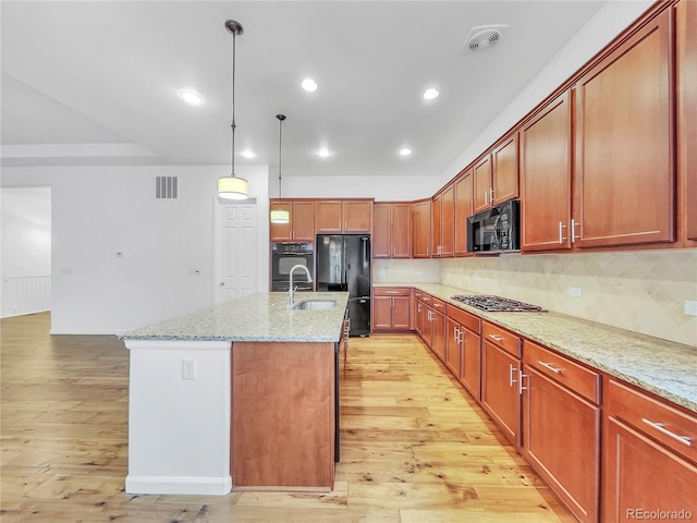 kitchen featuring black appliances, light stone counters, light hardwood / wood-style floors, and a center island with sink