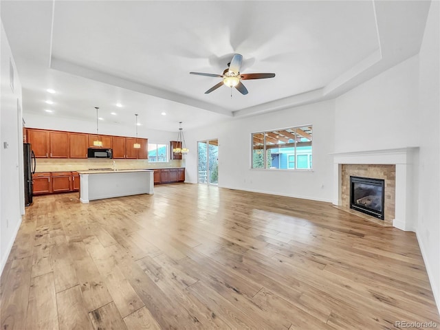 unfurnished living room with ceiling fan, a tile fireplace, and a tray ceiling