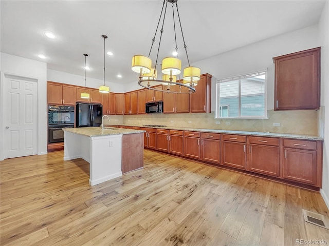 kitchen featuring decorative light fixtures, a center island with sink, black appliances, sink, and light stone countertops