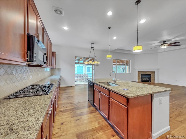 kitchen with light stone countertops, black appliances, decorative light fixtures, sink, and a kitchen island with sink