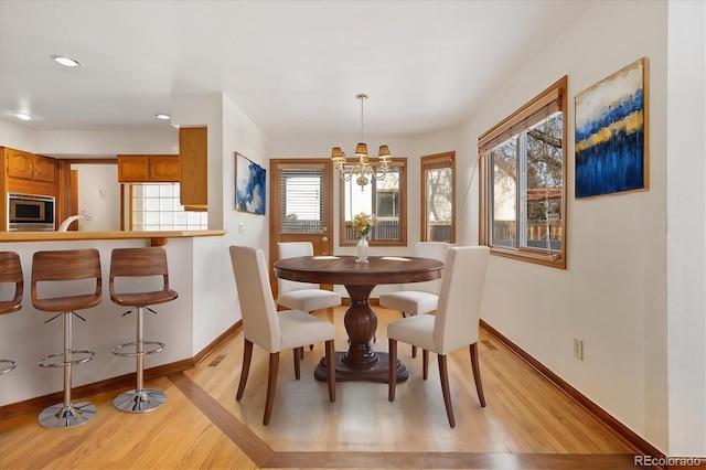 dining area with light wood-type flooring, a wealth of natural light, and an inviting chandelier