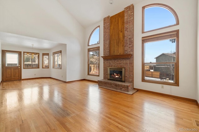 unfurnished living room with light wood-type flooring, a fireplace, high vaulted ceiling, and a notable chandelier