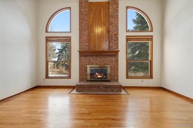 unfurnished living room with a fireplace, plenty of natural light, a high ceiling, and light hardwood / wood-style flooring