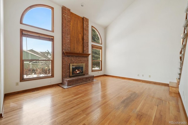 unfurnished living room featuring high vaulted ceiling, a brick fireplace, and light hardwood / wood-style flooring