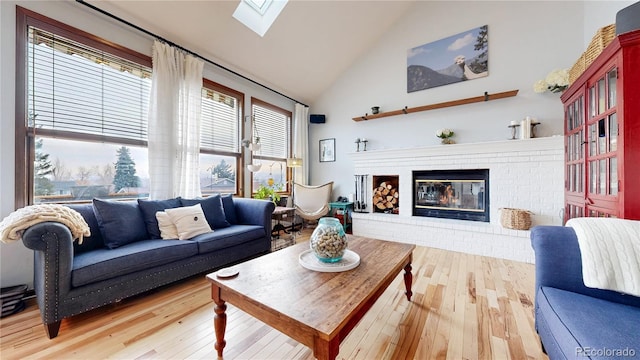 living area with a skylight, high vaulted ceiling, a brick fireplace, and wood finished floors