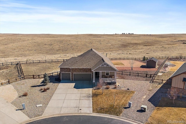 view of front of house featuring a garage, concrete driveway, a rural view, and fence