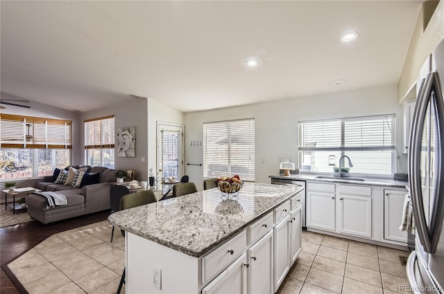 kitchen featuring a center island, white cabinets, sink, light stone countertops, and light tile patterned flooring