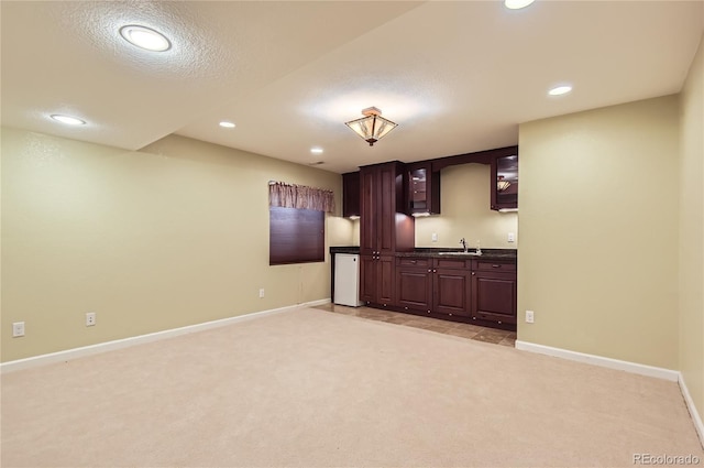 bar with dark brown cabinets, light colored carpet, a textured ceiling, and sink