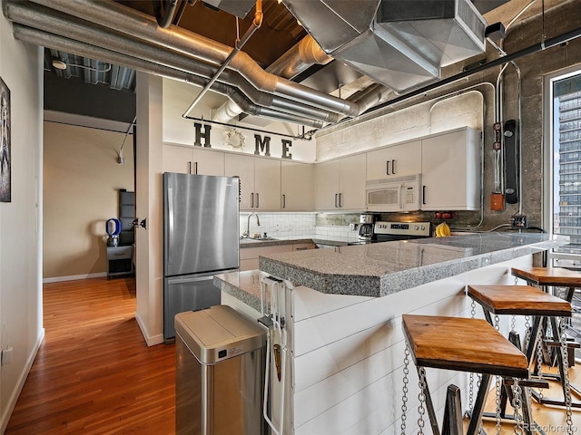 kitchen featuring a peninsula, appliances with stainless steel finishes, dark wood-style flooring, decorative backsplash, and baseboards