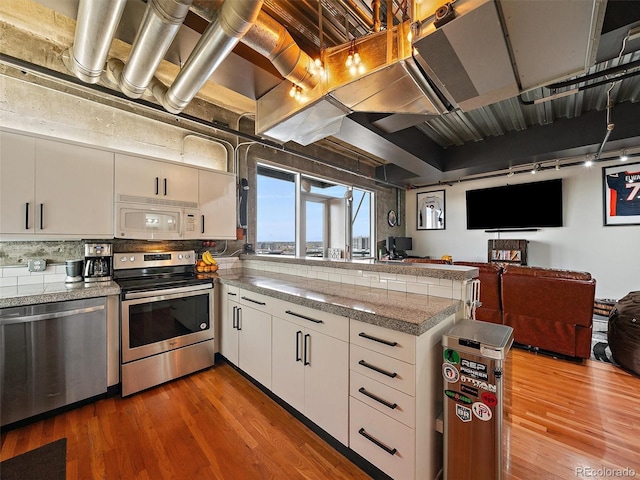 kitchen with a peninsula, white cabinetry, stainless steel appliances, open floor plan, and tile counters