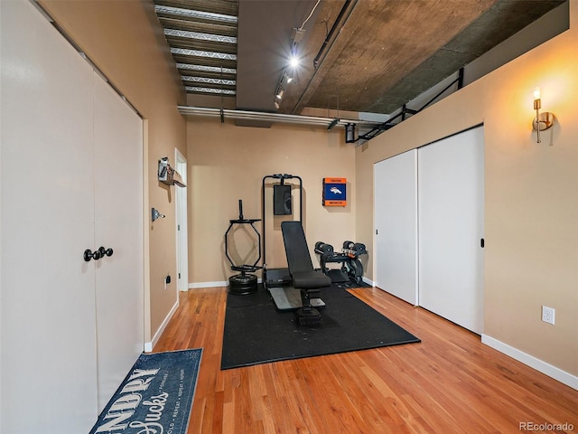 workout room featuring baseboards, a high ceiling, and wood finished floors