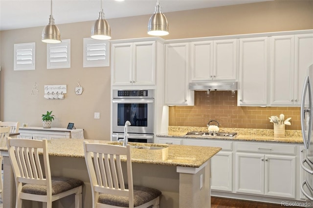 kitchen featuring decorative backsplash, appliances with stainless steel finishes, white cabinetry, a sink, and under cabinet range hood