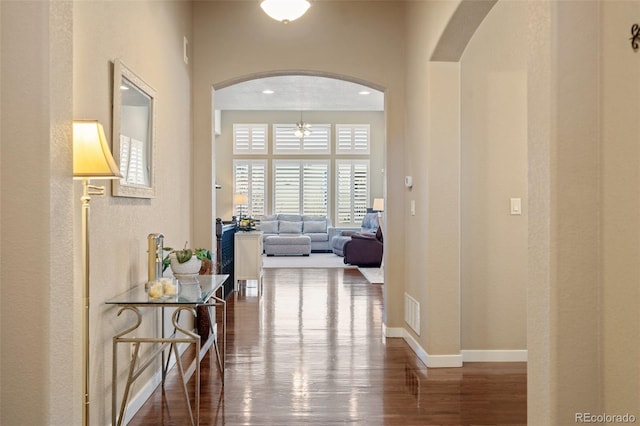 hallway with arched walkways, visible vents, baseboards, and wood finished floors