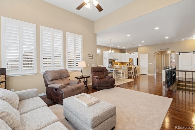 living room featuring arched walkways, recessed lighting, a barn door, dark wood-type flooring, and ceiling fan with notable chandelier