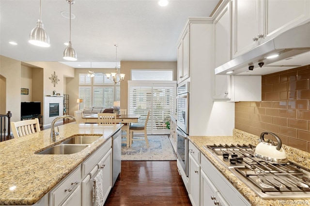 kitchen with dark wood finished floors, a glass covered fireplace, appliances with stainless steel finishes, under cabinet range hood, and a sink