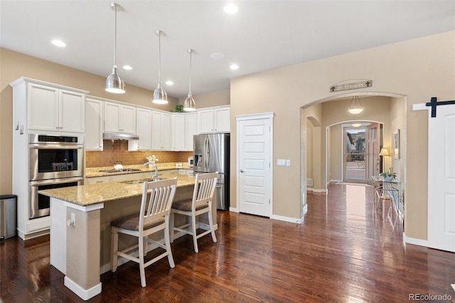 kitchen featuring arched walkways, light stone counters, stainless steel appliances, dark wood-style flooring, and backsplash